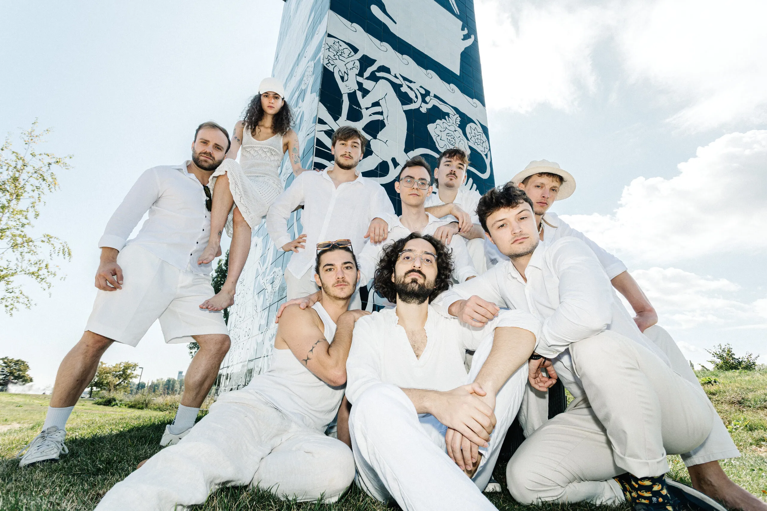 The nine musicians of Butter Bread dressed all in white on a lawn in front of a painted pillar
