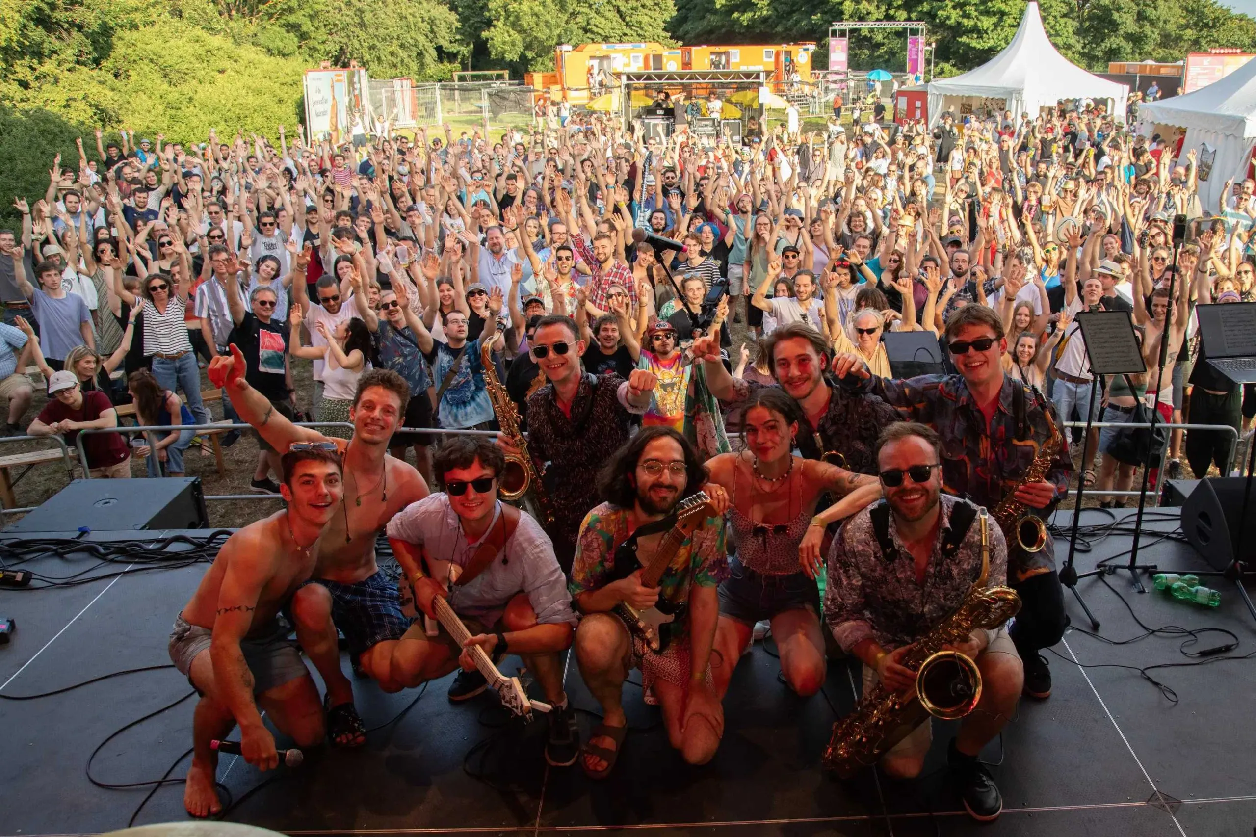 Group photo of the band on stage, a huge crowd behind them