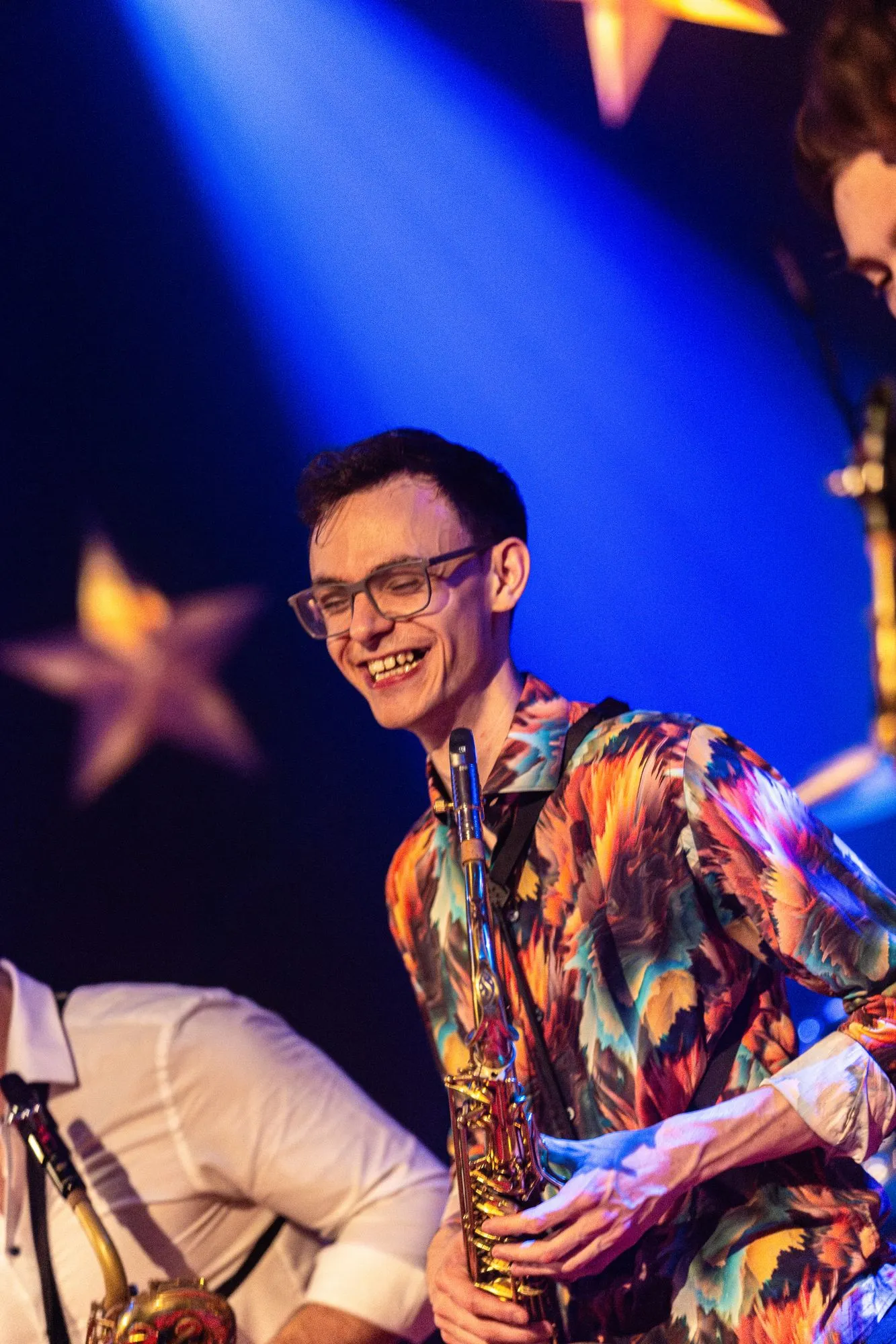 Saxofon im bunten Hemd, lachend im blauen Licht