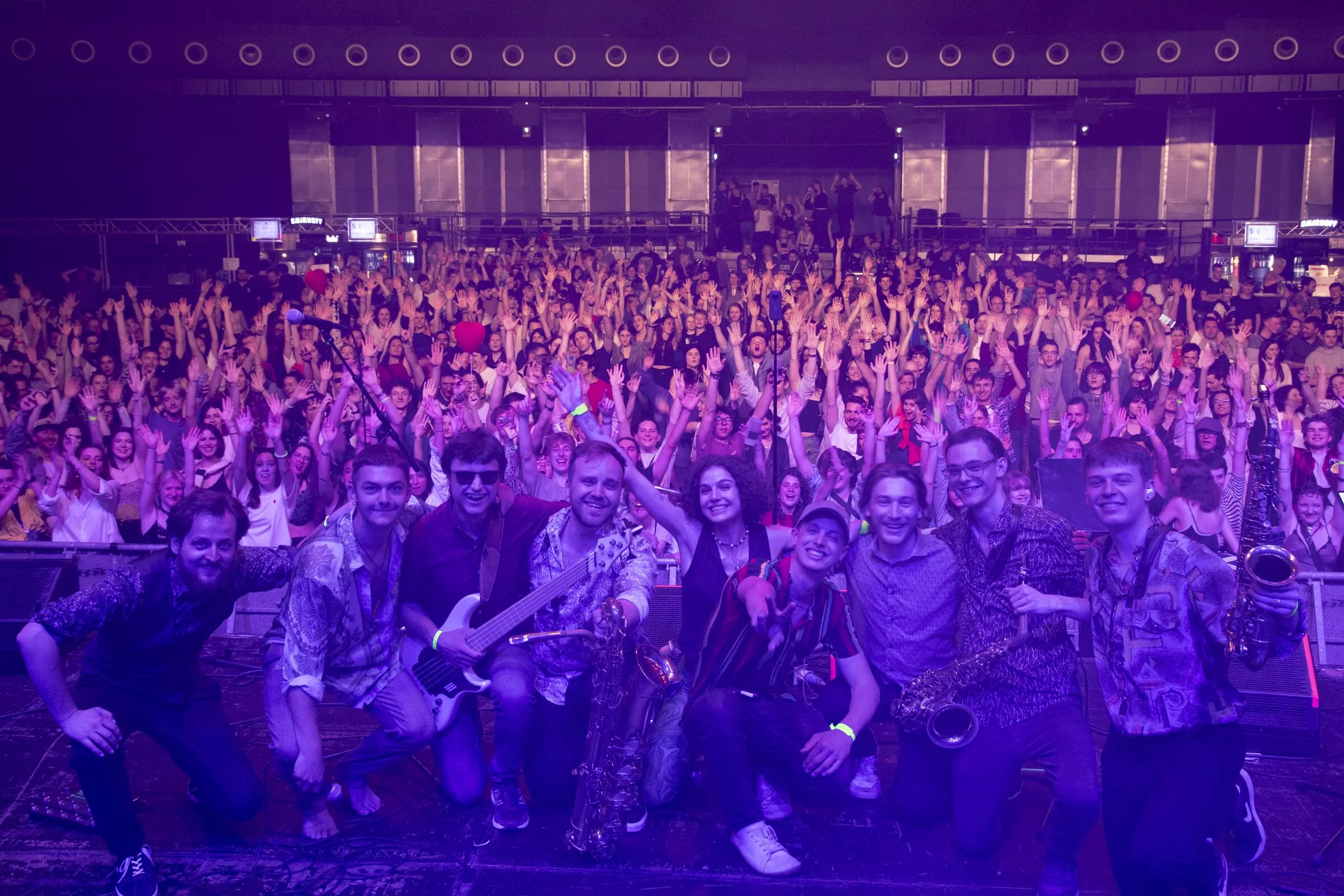 Gruppenfoto auf der Bühne vor dem vollen Saal in violettem Licht