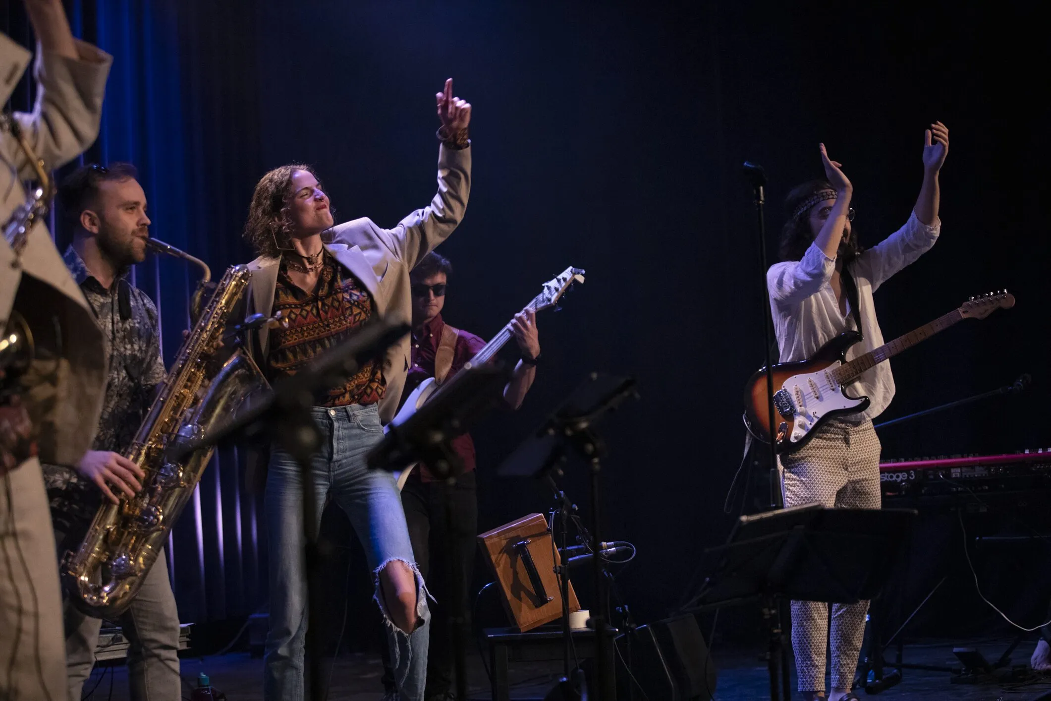 Saxofon, Gesang und Gitarre mit erhobenen Armen im Scheinwerferlicht